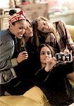 Four young women sitting on a sofa, smiling, taking a selfie, holding beer bottles.