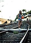 Young woman standing on railway tracks holding a basketball.