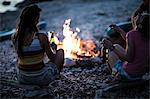 A group of young people gathered on a beach around a campfire..