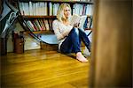 Woman sitting on floor reading book at home