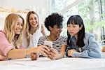 Young women laughing at multimedia smartphone in cafe