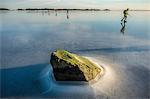 Stone peaking through the ice and ice-skaters