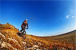 Wide angle view of a cyclist riding a bike on a nature trail in the mountains. people living a healthy lifestyle. Cyclist with helmet and gjasses. Beautiful landscape with hill and blue sky. Spring season. Travel in the countryside.