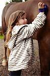 Girl brushing horse's coat outdoors