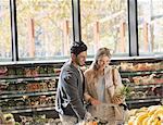 Smiling young couple grocery shopping, holding pineapple in market