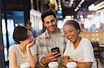 Young friends using cell phone, texting and laughing at cafe