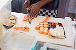 Young female chef slicing salmon, making sushi in restaurant