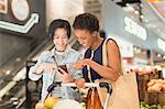 Young lesbian couple using cell phone, grocery shopping in market