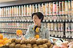 Young woman with headphones grocery shopping, holding orange in market
