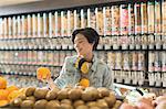 Young woman with headphones grocery shopping, holding orange in market