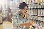 Smiling young woman with headphones talking on cell phone grocery shopping in market