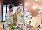 Female worker helping young couple at deli counter in grocery store market