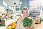 Portrait smiling young woman holding bunch of kale in grocery store market