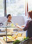 Smiling young woman helping customer at cheese counter in grocery store market