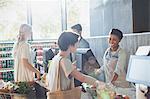 Smiling female cashier helping customer at grocery store checkout