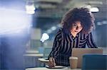 Focused businesswoman working late at laptop, taking notes in dark office