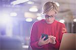 Businesswoman working late at laptop, texting with cell phone in dark office