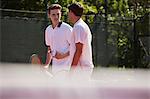 Male tennis players with tennis rackets talking on sunny tennis court