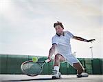 Determined young male tennis player playing tennis, reaching for the ball on sunny tennis court