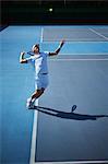 Young male tennis player playing tennis, serving the ball on sunny blue tennis court