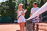 Smiling male and female tennis players talking at tennis net on sunny clay tennis court