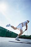 Young male tennis player playing tennis, swinging racket on sunny tennis court