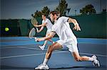 Young male tennis doubles players playing tennis, hitting the ball on blue tennis court