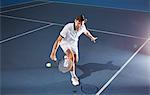 Young male tennis player playing tennis, reaching with tennis racket on blue tennis court