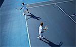 Young male doubles tennis players playing tennis on sunny blue tennis court