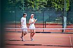 Young tennis player couple walking with tennis rackets on sunny clay tennis court