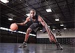 Portrait confident young male basketball player dribbling the ball on court in gymnasium