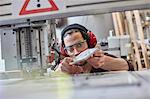 Male designer wearing ear protectors, examining prototype in workshop