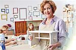 Portrait confident mature female artist holding painted bench in art class workshop