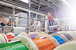 Male worker with clipboard checking multicolor spools in fiber optics factory