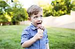 Preschool boy eating ice cream cone in summer yard