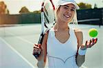 Portrait smiling, confident young female tennis player holding tennis racket and tennis ball on tennis court