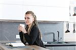 attractive woman having an hot drink while reading a book relaxing in her kitchen even if she could use a smartphone or her tablet, but she prefers to read and educate her mind