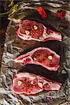 Three Raw Pork Steaks with Spices on Parchment Paper. Vertical.