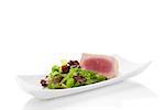 Delicious tuna steak with fresh green salad on white plate isolated on white background. Culinary seafood eating.