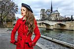 Bright in Paris. elegant traveller woman in red trench coat on embankment near Notre Dame de Paris in Paris, France