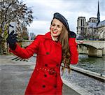 Bright in Paris. happy trendy tourist woman in red trench coat on embankment in Paris, France with cellphone taking selfie