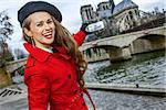 Bright in Paris. happy trendy woman in red trench coat on embankment near Notre Dame de Paris in Paris, France with mobile phone taking photo