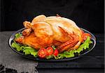 Roasted chicken on black background with lettuce and tomatoes