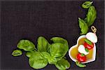 Culinary caprese background.. Mozzarella cheese, fresh basil and cherry tomatoes with extra virgin olive oil, top view. Traditional italian eating.