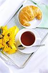 Morning breakfast with croissant, tea and yellow roses on vintage silver  tray.