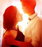 Young people hugging in the apartment in the evening in the rays of the sunset. A loving couple on a date on a summer evening. The guy with the girl hugs and kisses. Youth, first feelings, first love, first dates. faces close up. Sun flares in the frame and shallow depth of field create a romantic mood