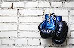 Pair of old blue and black boxing gloves hanging on white brick wall.