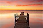 Stunning vivid red sunrise and timber jetty with reflections of the beautiful sky in the waters.  Gorokan jetty, Australia