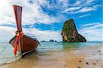 A wooden Thai boat with a motor on the background of a high cliff in the Andaman Sea