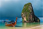 Traditional wooden Thai boat near the shore and high cliff